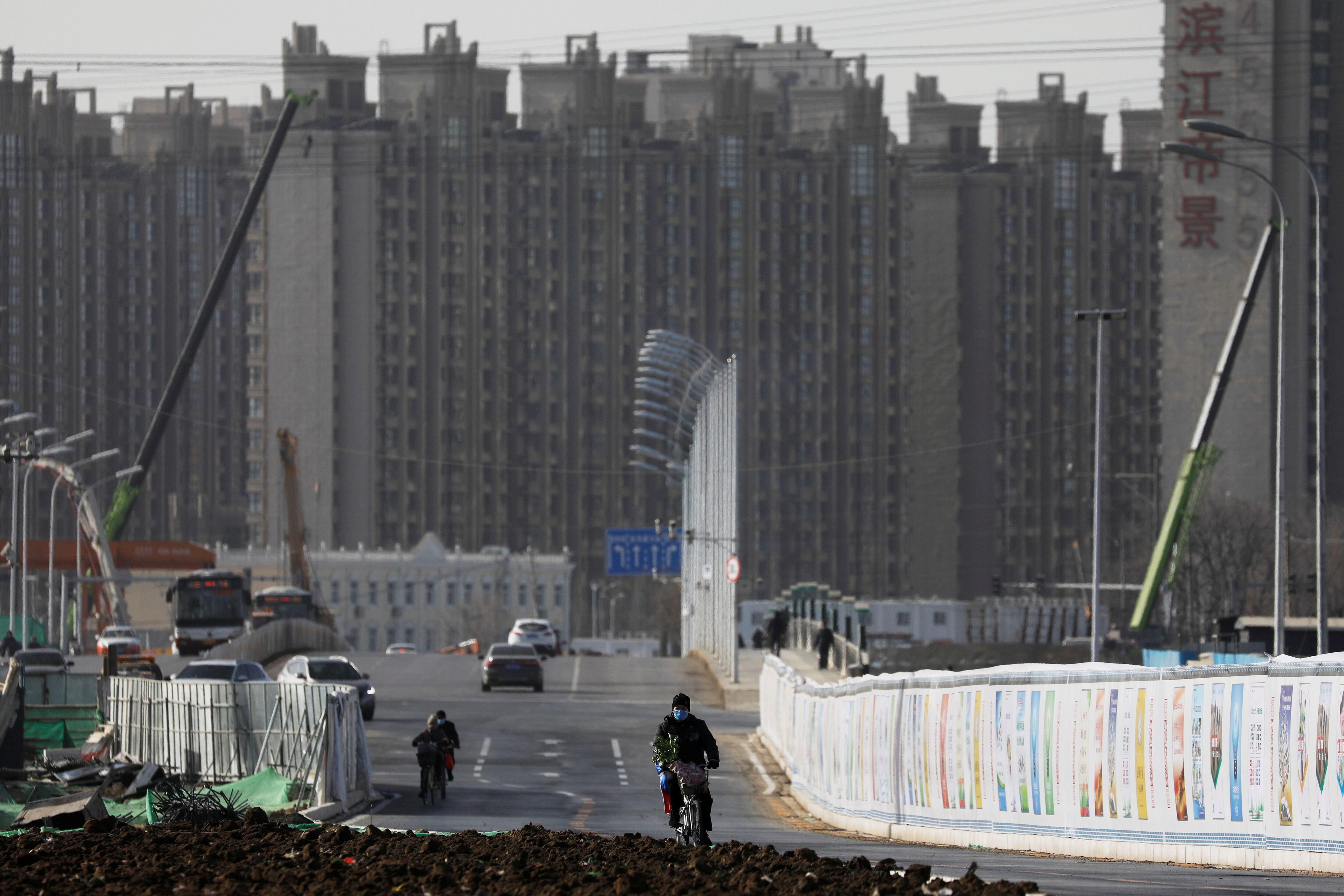 Un hombre anda en bicicleta junto a un sitio de construcción cerca de edificios residenciales en Beijing, China, el 13 de enero de 2021. (REUTERS/Tingshu Wang)