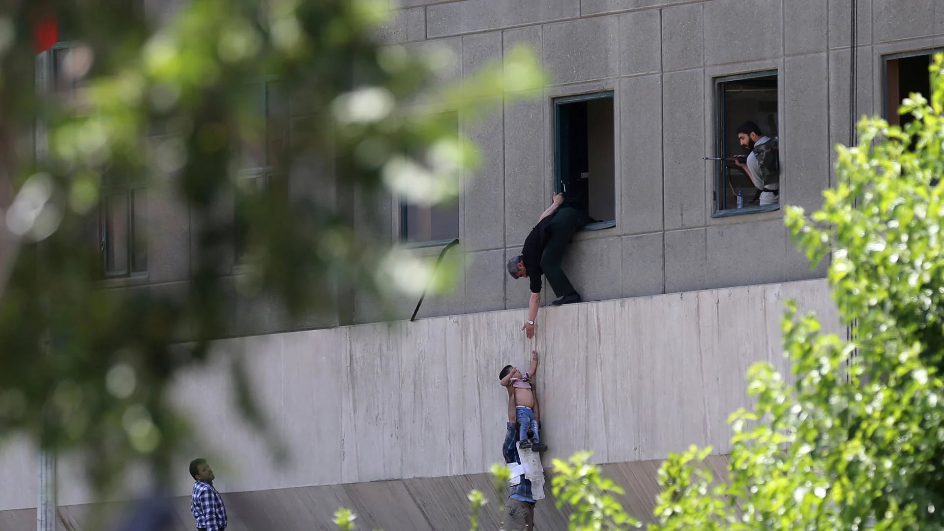 Varias personas ayudan a evacuar a niño desde una ventana del Parlamento iraní, en Teherán, en medio de la toma de rehenes tras un ataque comando (AP)
