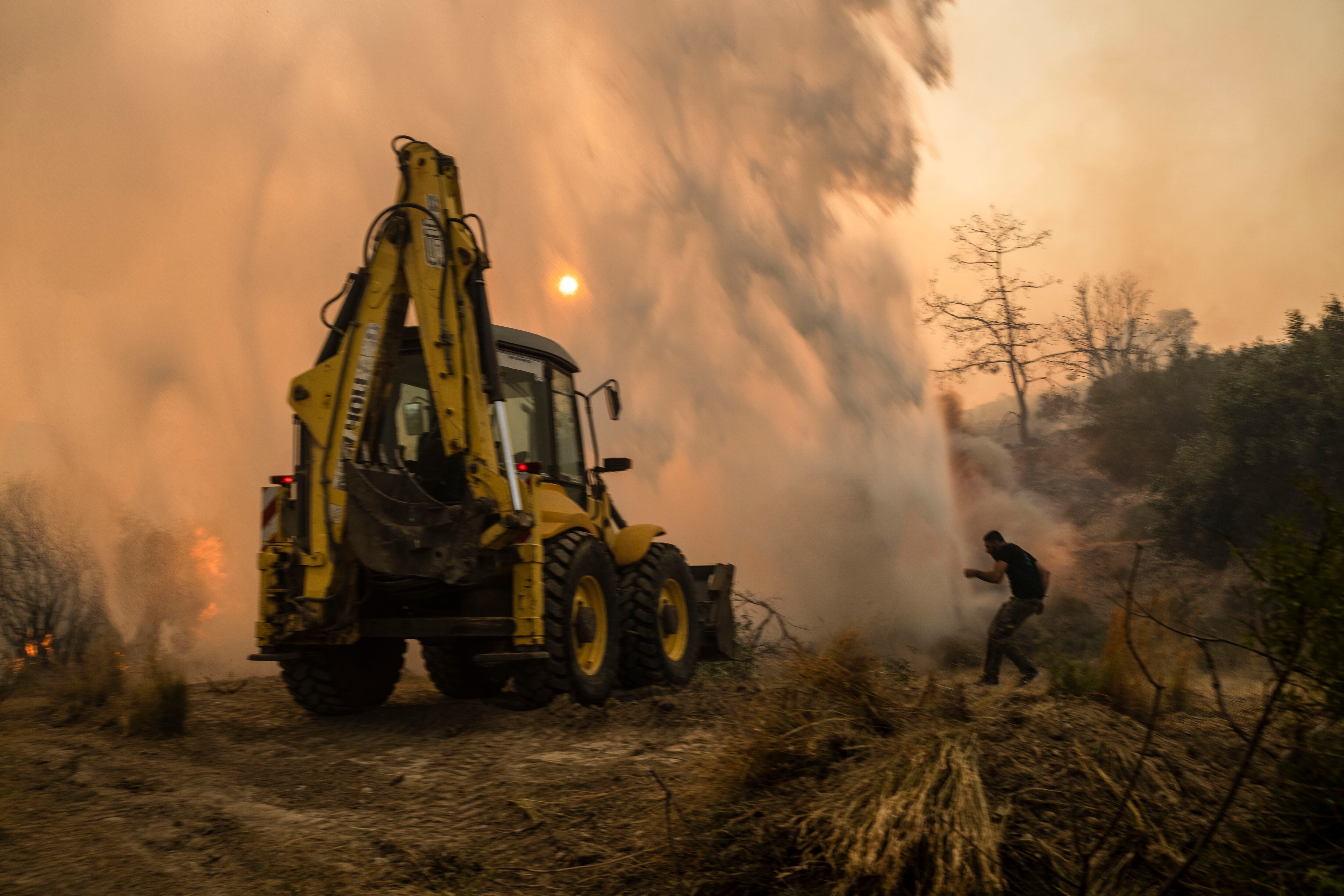Un vecino trata de evitar el agua arrojada por un helicóptero durante las labores de extinción de un incendio en Gennadi. (AP Foto/Petros Giannakouris)