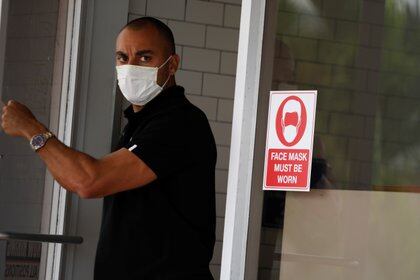 Un hombre sale de un restaurante junto a un letrero que indica que debe usar una máscara facial, en Miami