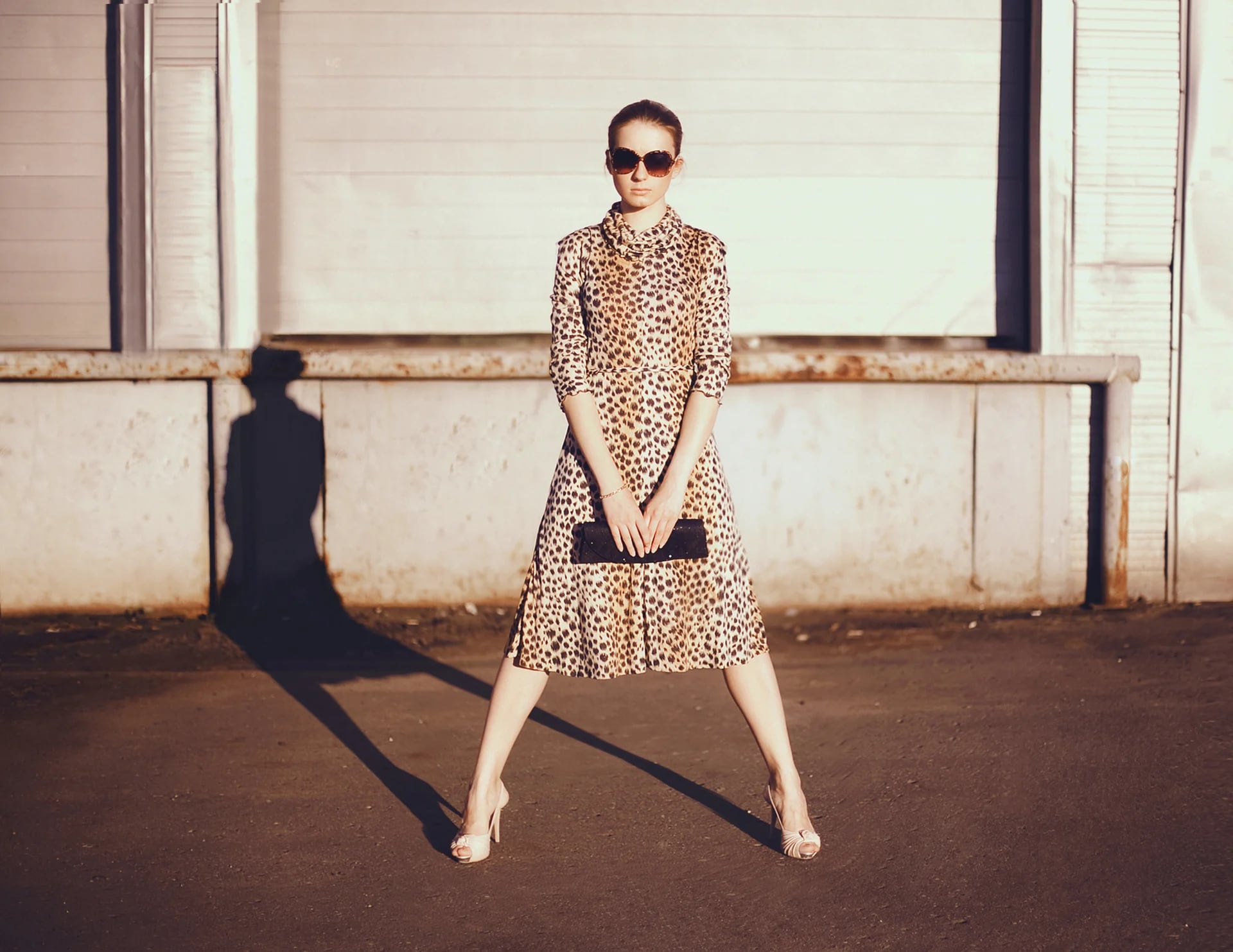 Stylish woman in a leopard dress, glasses and bag in the ghetto evening, street fashion.