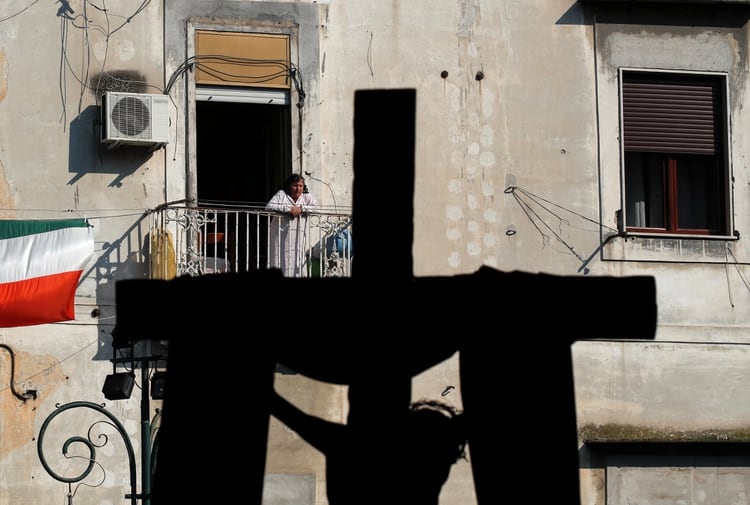 Una mujer observa desde su balcón un crucifijo expuesto fuera de la iglesia de Santa María de la Sanita durante el Viernes Santo, ya que Italia permanece encerrada durante el período de Pascua para tratar de contener la propagación de la enfermedad coronavirus (COVID-19), en Nápoles, Italia, el 10 de abril de 2020 (Reuters)