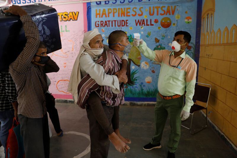 Un trabajador lleva a su padre a la espalda se hace controlar la temperatura antes de inscribirse en un tren hacia su estado natal de Uttar Pradesh, en Nueva Delhi, India, el 26 de mayo de 2020. REUTERS/Adnan Abidi