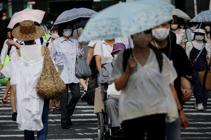 Transeúntes con máscaras faciales protectoras y sombrillas se ven en medio del brote de coronavirus en las calles en Tokio, Japón (Reuters)
