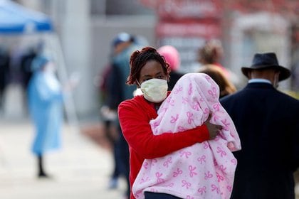 Una mujer sostiene a un bebé mientras camina junto a gente que espera en línea para realizarse exámenes durante el brote global de COVID-19, la enfermedad causada por el nuevo coronavirus, afuera del Roseland Community Hospital en Chicago, Illinois, Estados Unidos [7 de abril de 2020] (Reuters/ Joshua Lott)