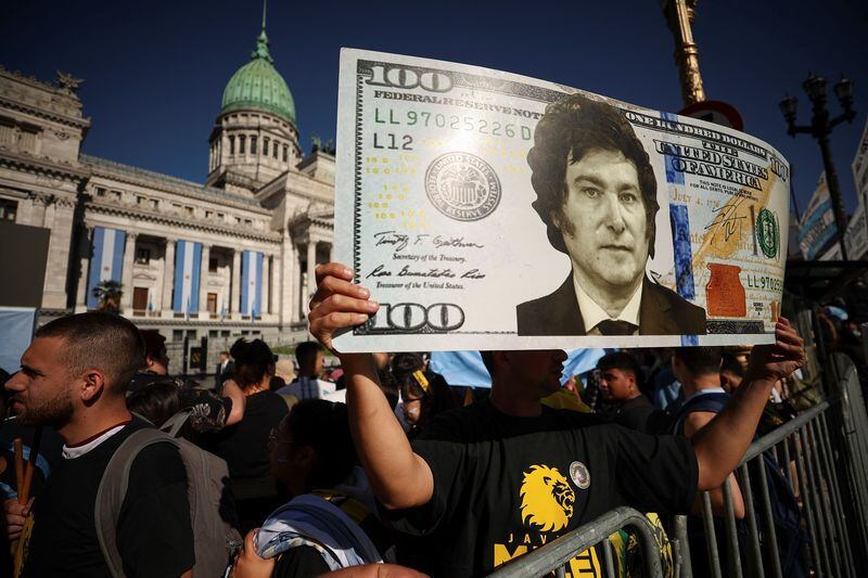 Un seguidor del presidente electo de Argentina Javier Milei sostiene la representación de un billete de 100 dólares con su imagen. REUTERS/Agustin Marcarian