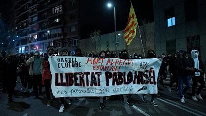 Protesters march with a banner reading "Freedom to (Spanish rapper) Pablo Hasel" during a demonstration in Barcelona against his arrest on February 16, 2021. - Spanish police stormed a university to arrest the rapper barricaded inside after being sentenced to nine months' jail over tweets attacking the monarchy and the police in a case denounced as an attack on freedom of speech. (Photo by Josep LAGO / AFP)