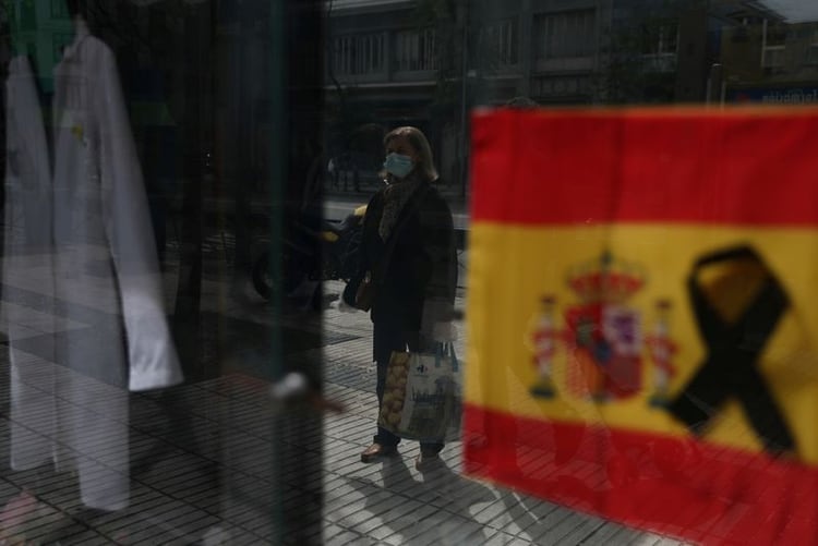 Una mujer con una máscara protectora espera entrar en una farmacia mostrando una bandera española con un lazo negro, en medio del brote de la enfermedad coronavirus (COVID-19) en Madrid, España, el 18 de abril de 2020. REUTERS/Susana Vera/Archivo Foto