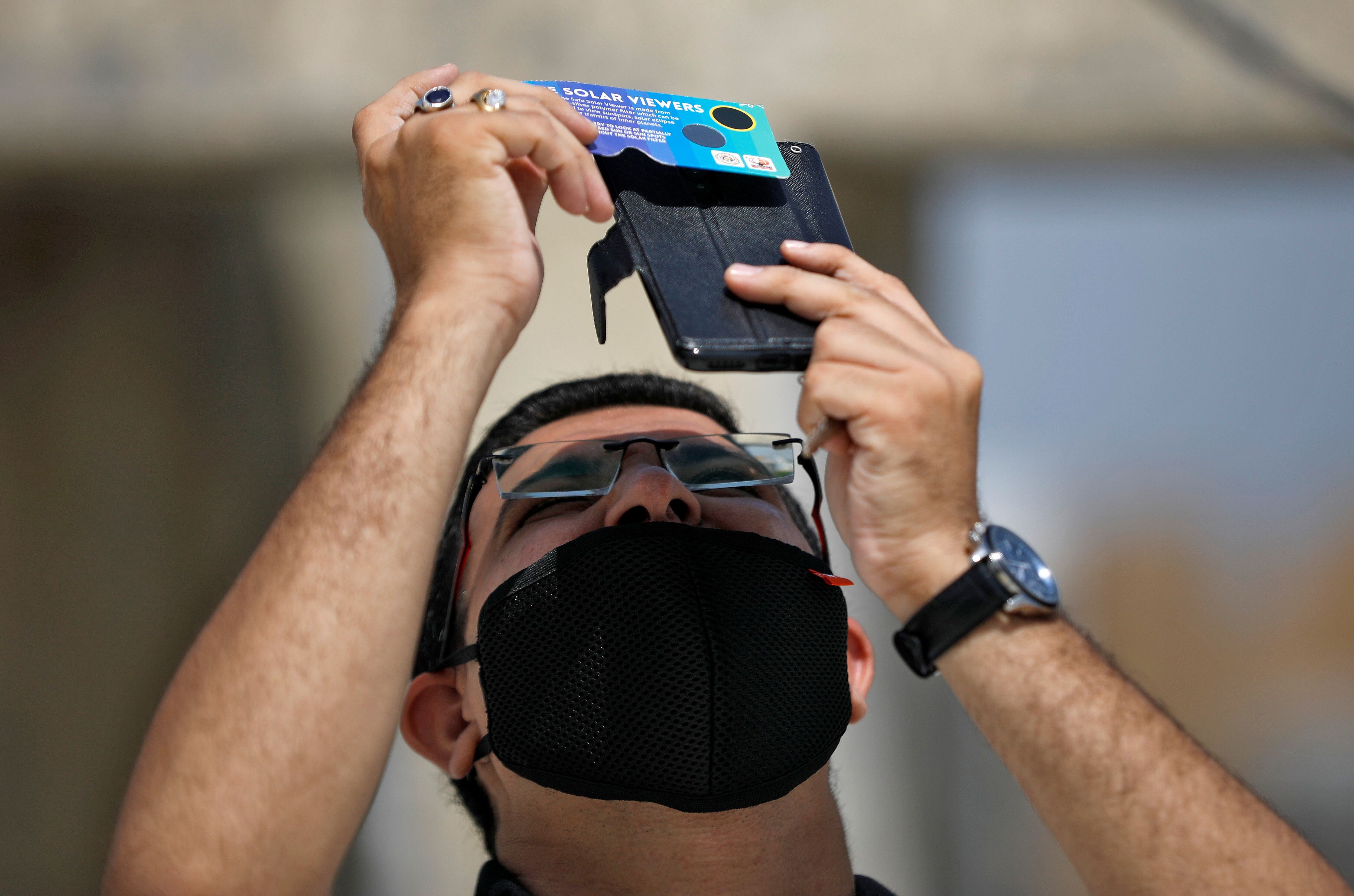 A man, wearing a protective face mask against the coronavirus disease (COVID-19), uses his mobile phone and solar viewers to take photographs of a partial solar eclipse at Gandhinagar, India, June 21, 2020. REUTERS/Amit Dave
