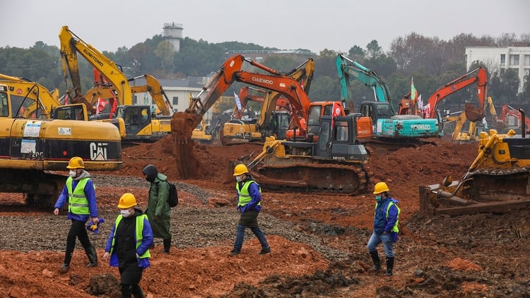 Los trabajadores caminan para dar paso a decenas de palas mecánicas y otras máquinas que construyen el hospital (Chinatopix vía AP)