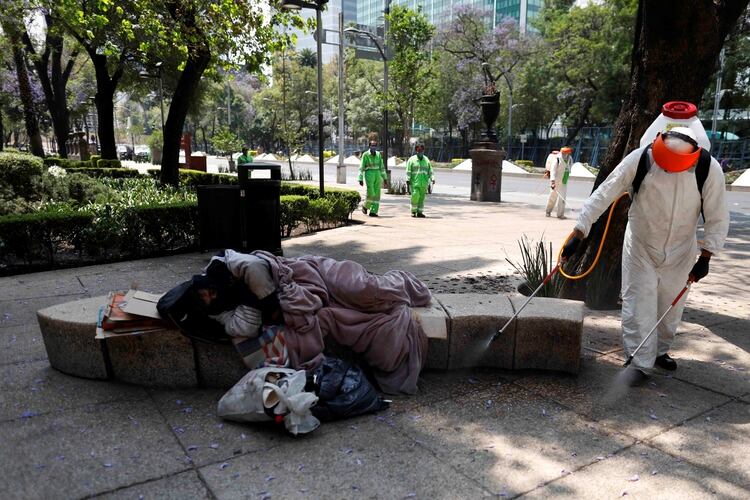 una persona sin hogar duerme en una banca mientras empleados de limpieza desinfectan la avenida Reforma, en la Ciudad de México REUTERS/Carlos Jasso