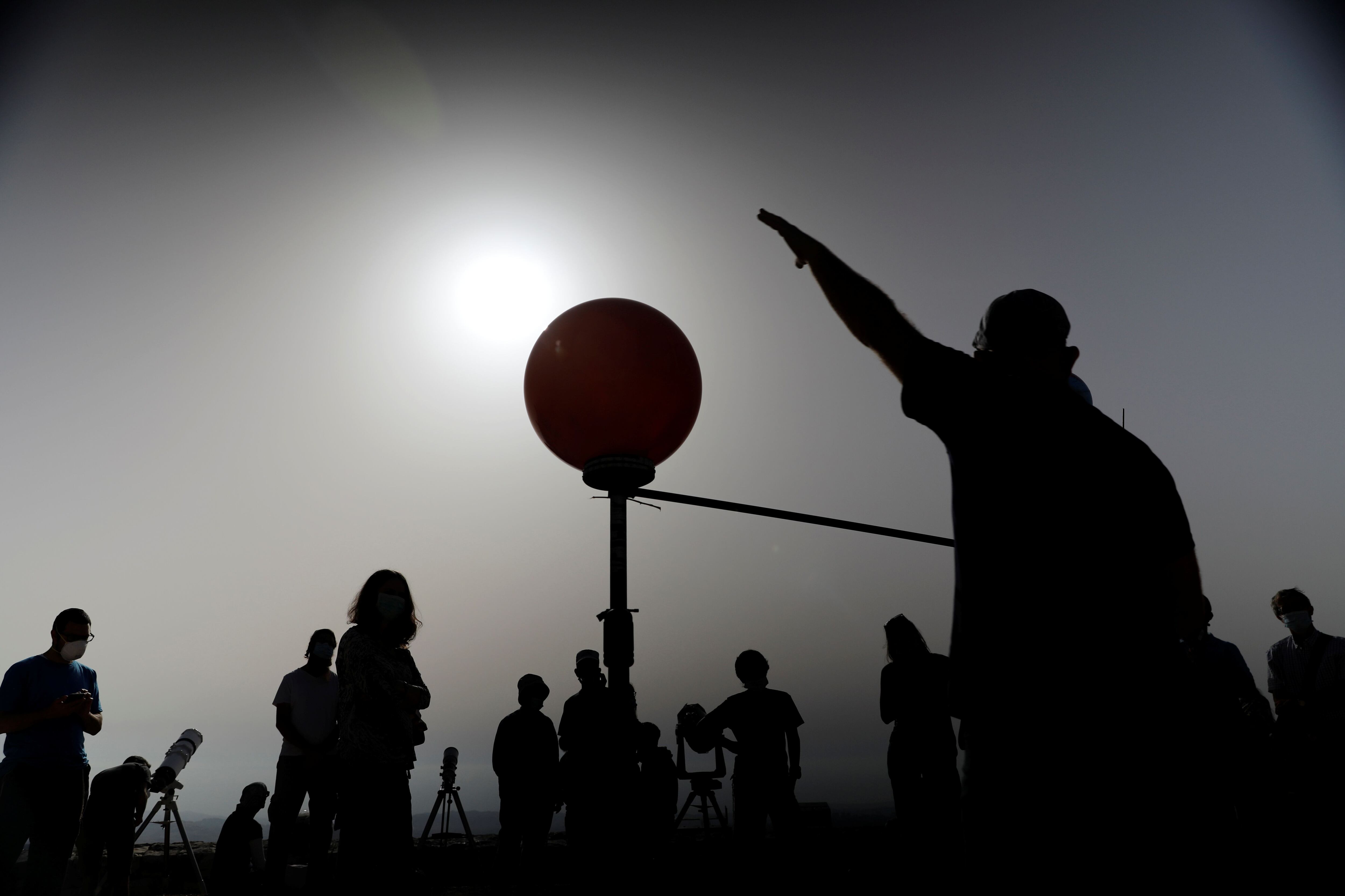 People stand next to a model of the earth, the moon and the sun as a partial solar eclipse is seen from Mount Scopus in Jerusalem June 21, 2020. REUTERS/Ronen Zvulun