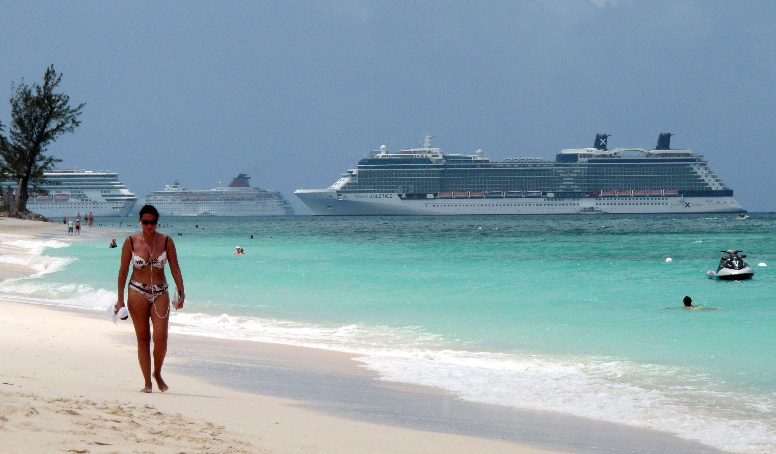 Una mujer camina a lo largo de la playa Seven Mile con tres cruceros anclados en el puerto de George Town, Islas Caimán, cuando la pandemia por coronavirus aún permitía el turismo en las islas (Reuters)