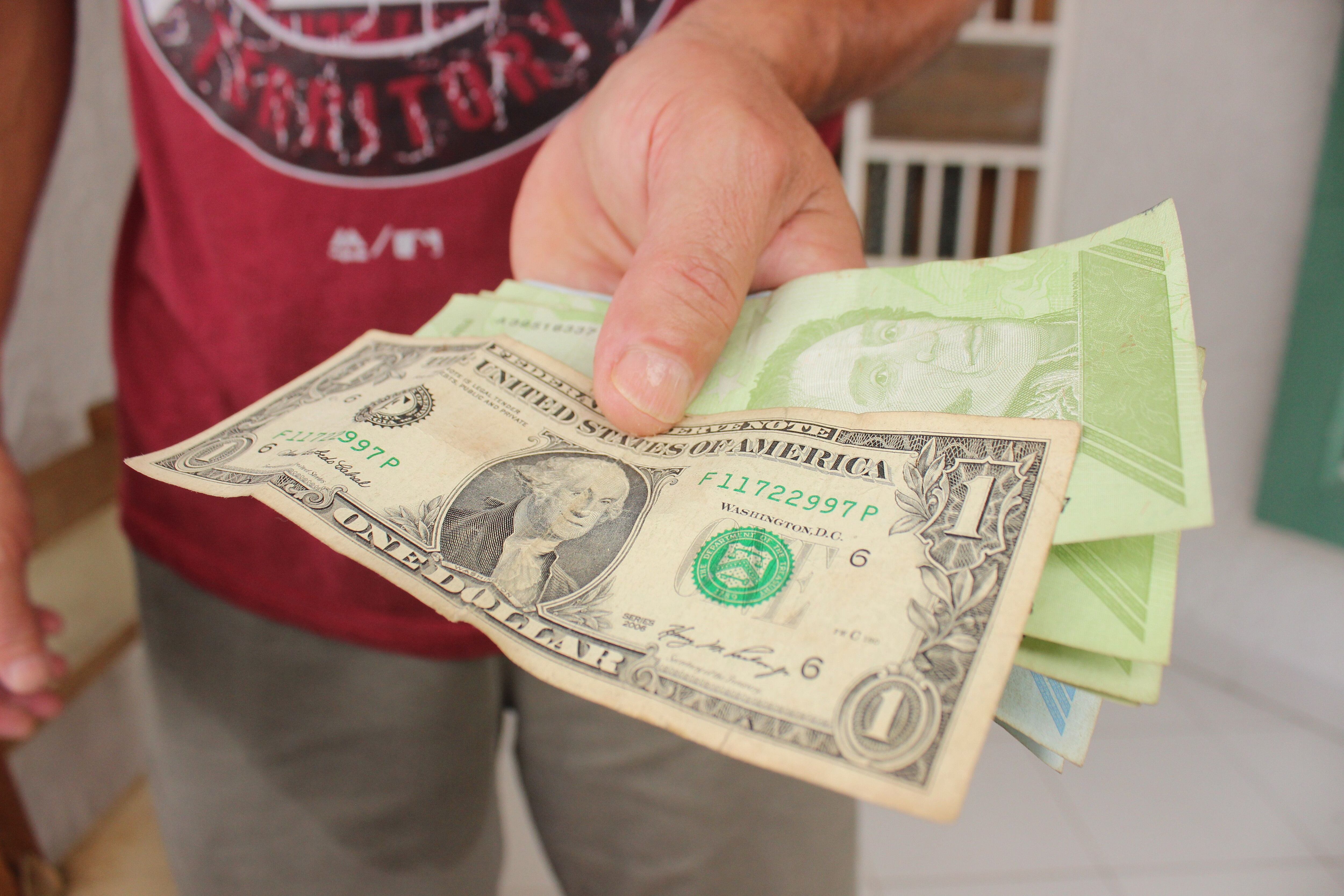 Fotografía de archivo en la que se registró la mano izquierda de un hombre al sostener un fajo de bolívares de distintas denominaciones, bajo un billete de dólar, en San Cristóbal (Táchira, Venezuela). EFE/Johnny Parra 