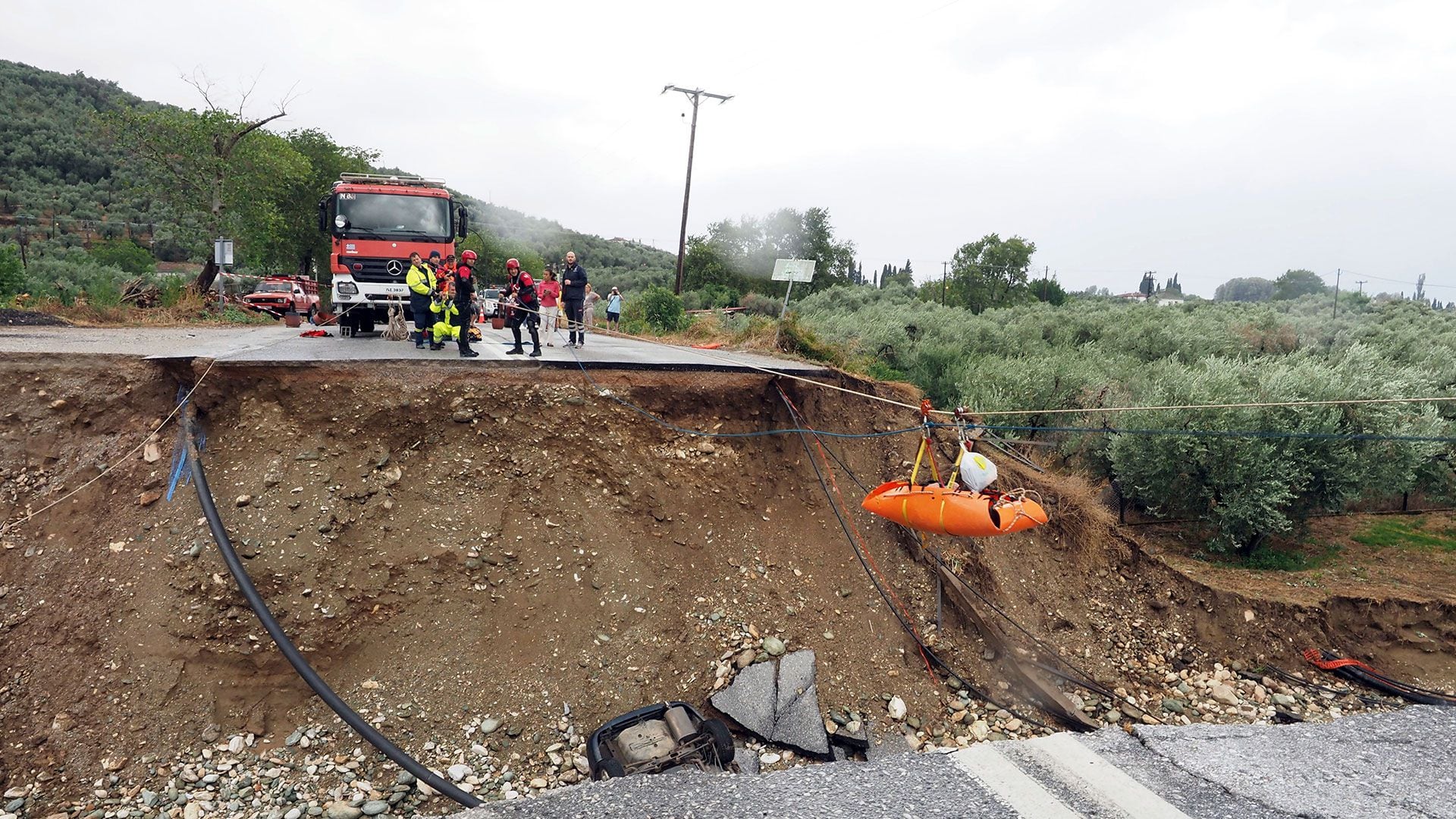 Los bomberos utilizan cuerdas para levantar a un paciente renal en una camilla a través de una carretera dañada  (AP/Thodoris Nikolaou)