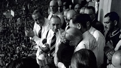 Perón abraza a Evita tras anunciar ella que no será candidata a vicepresidente. A la izquierda, aplaude Héctor Cámpora (Foto: Pinélides Aristóbulo Fusco)