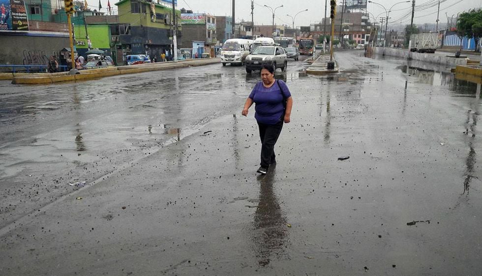 Una ciudadana peruana cruza la pista en una concurrida avenida capitalina en plena lluvia de otoño, para llegar a su domicilio.