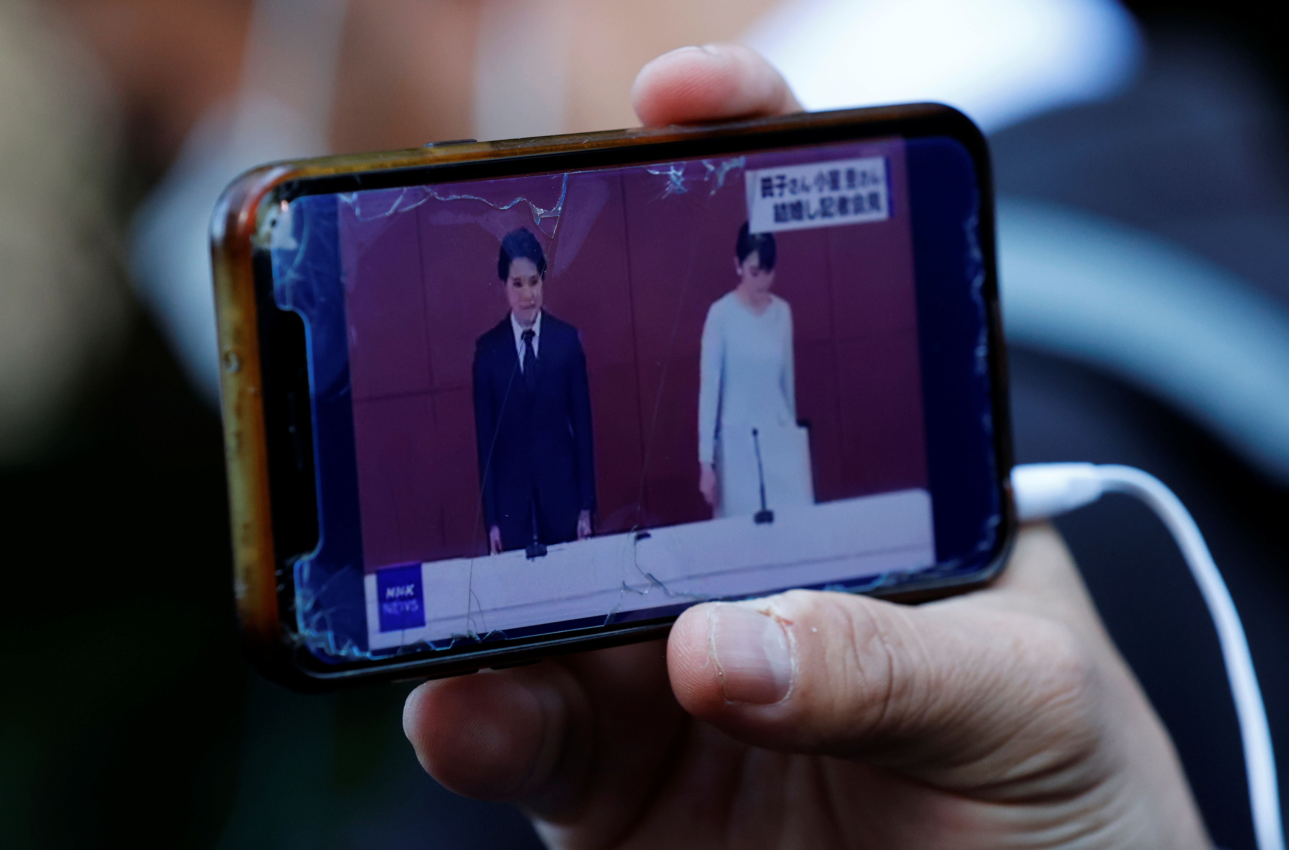 Un hombre mira una transmisión en vivo de la conferencia de prensa de la princesa Mako de Japón y su esposo Kei Komuro en un teléfono inteligente, afuera de un hotel donde se llevará a cabo la conferencia de noticias en Tokio, Japón, el 26 de octubre de 2021. REUTERS / Kim Kyung-Hoon