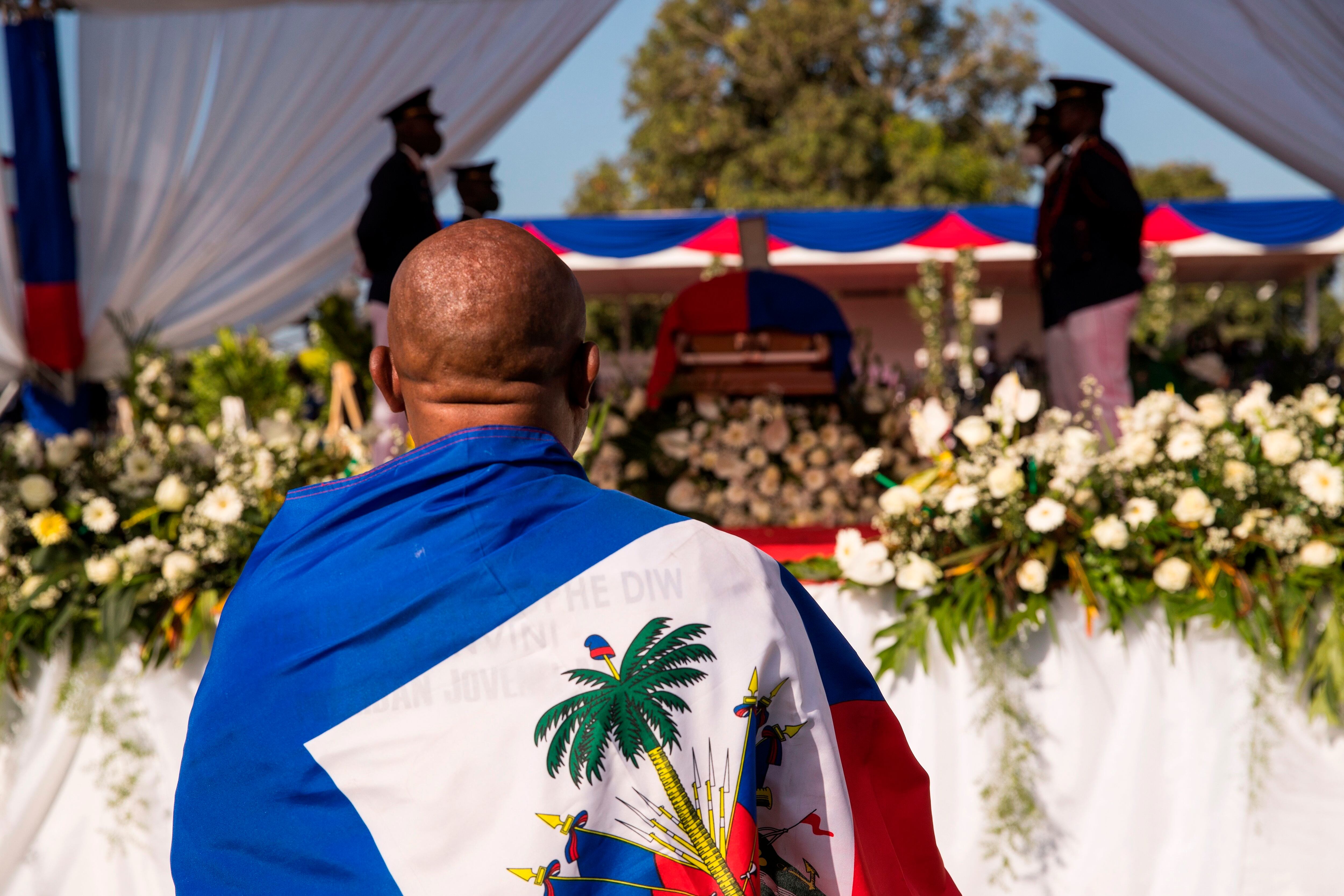 Un hombre envuelto con la bandera nacional observa el féretro del presidente Jovenel Moise, durante su ceremonia fúnebre. EFE/ Orlando Barria/Archivo