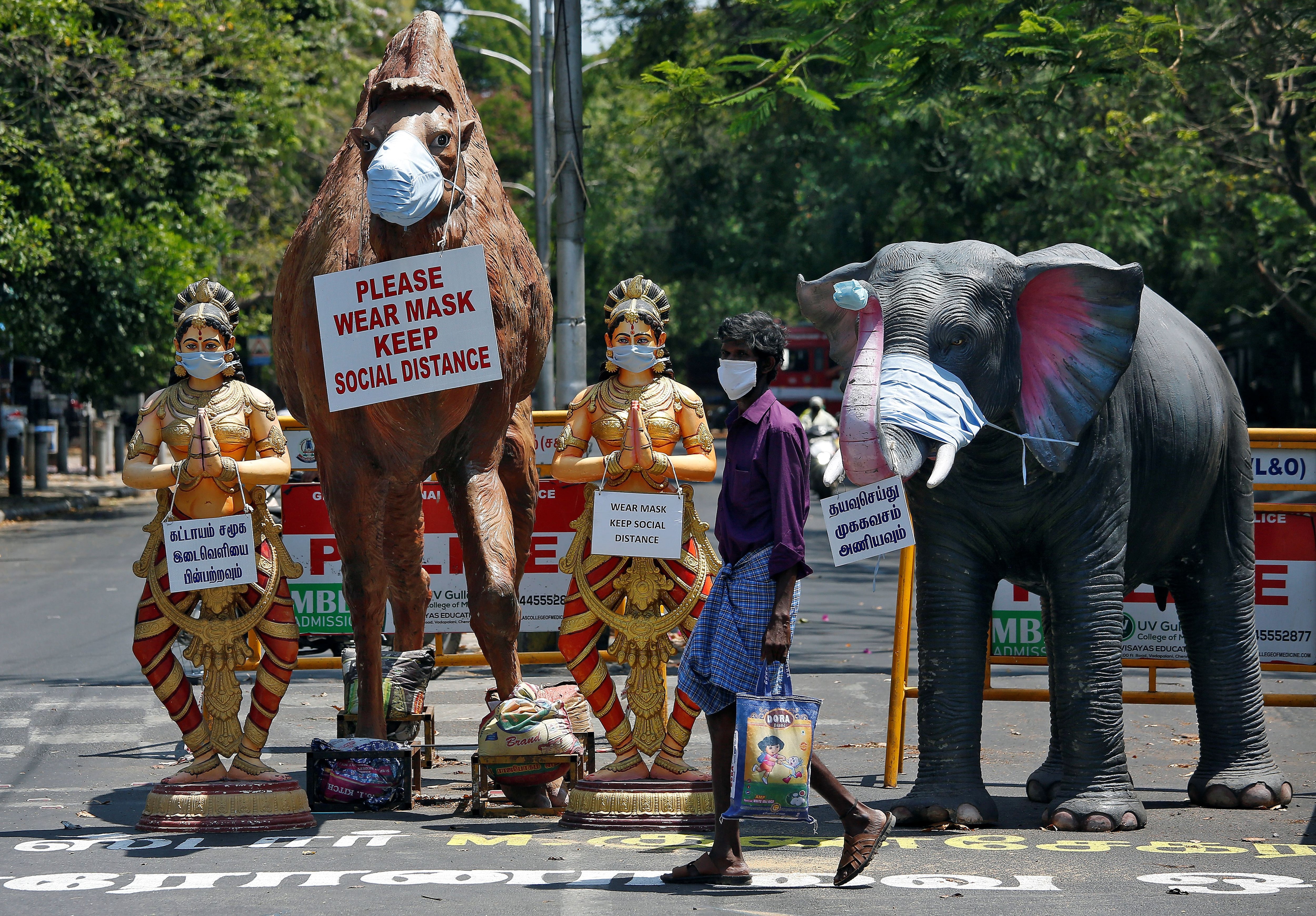 Un hombre con una máscara protectora pasa por delante de réplicas de animales y bailarines tradicionales instalados en un cruce de carretera, para crear conciencia sobre el uso de máscaras en Chennai, India, el 23 de abril de 2020. REUTERS/P. Ravikumar