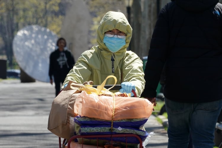 Una mujer con una máscara y una capucha camina con su carrito de compras durante el brote de coronavirus en Harlem, Manhattan (Reuters)