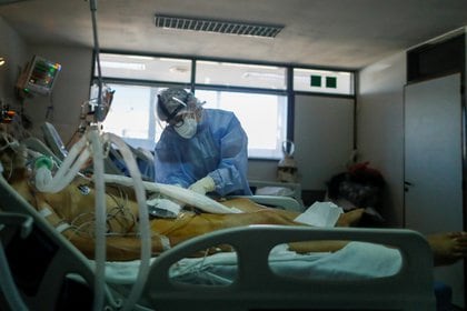 Un trabajador de la salud revisa a un paciente que padece la enfermedad del coronavirus (COVID-19), en una unidad de cuidados intensivos de un hospital en las afueras de Buenos Aires, Argentina, 16 de abril de 2021. Fotografía tomada a través de un cristal. REUTERS / Agustin Marcarian