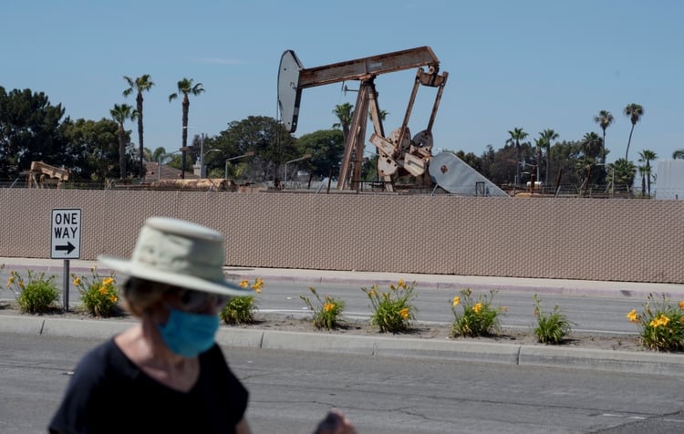 Un peatón con una máscara protectora pasa junto a una torre de perforación de petróleo en Huntington Beach Fotografía tomada el 25 de abril de 2020. (REUTERS / Kyle Grillot)