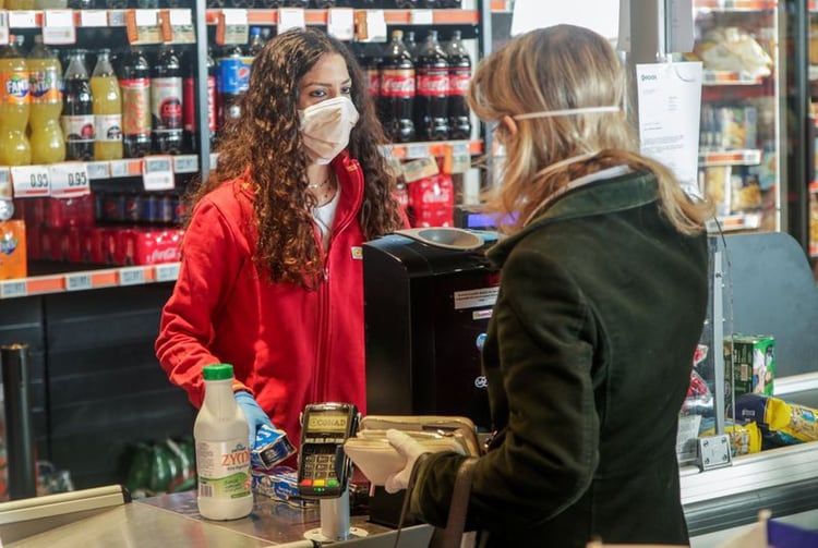 Una trabajadora de un supermercado que usa una máscara facial protectora atiende a una cliente en Nápoles, Italia, el 10 de marzo de 2020. REUTERS/Ciro De Luca