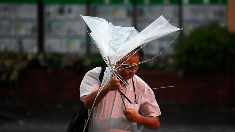Un hombre con un paraguas cruza una calle temprano en la mañana bajo la lluvia. (Foto por Charly TRIBALLEAU / AFP)