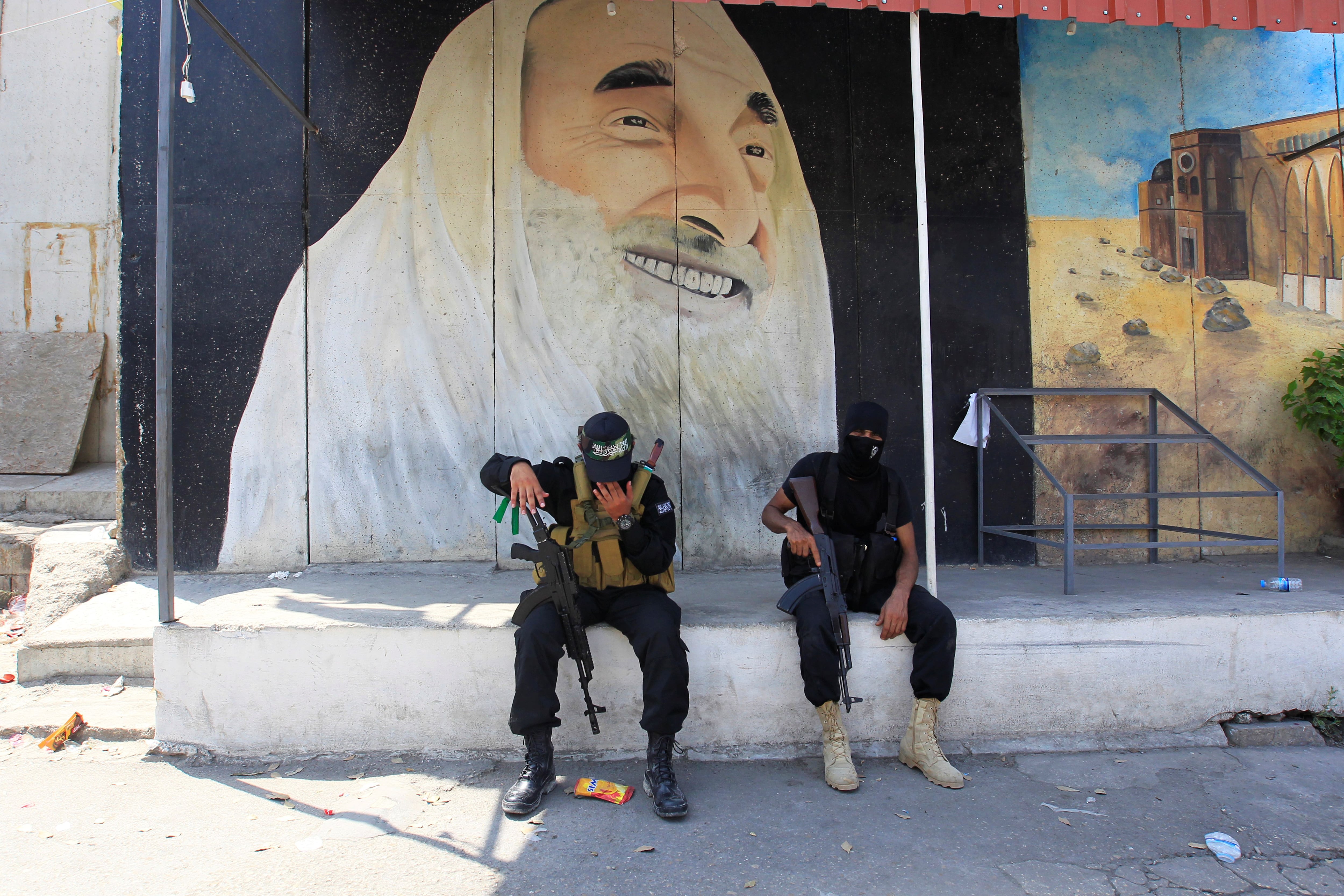 Terroristas palestinos están sentados frente a un mural de Ahmed Yassin, líder espiritual de Hamas, que fue abatido en un operativo de Israel (REUTERS/Aziz Taher)