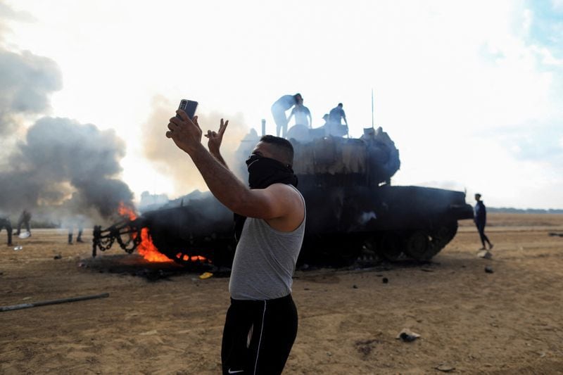 Un terrorista palestino se saca una selfie delante de un vehículo militar israelí en llamas tras ser alcanzado por atacantes de Hamas que se infiltraron en zonas del sur de Israel, en el lado israelí de la frontera entre Israel y Gaza, el 7 de octubre de 2023 (Reuters)
