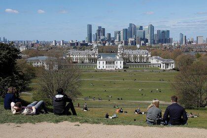 Visitantes en el Greenwich Park se sientan y miran hacia el distrito financiero de Canary Wharf mientras se alivian las restricciones en medio de la propagación de la pandemia de COVID-19 en Londres (Reuters)