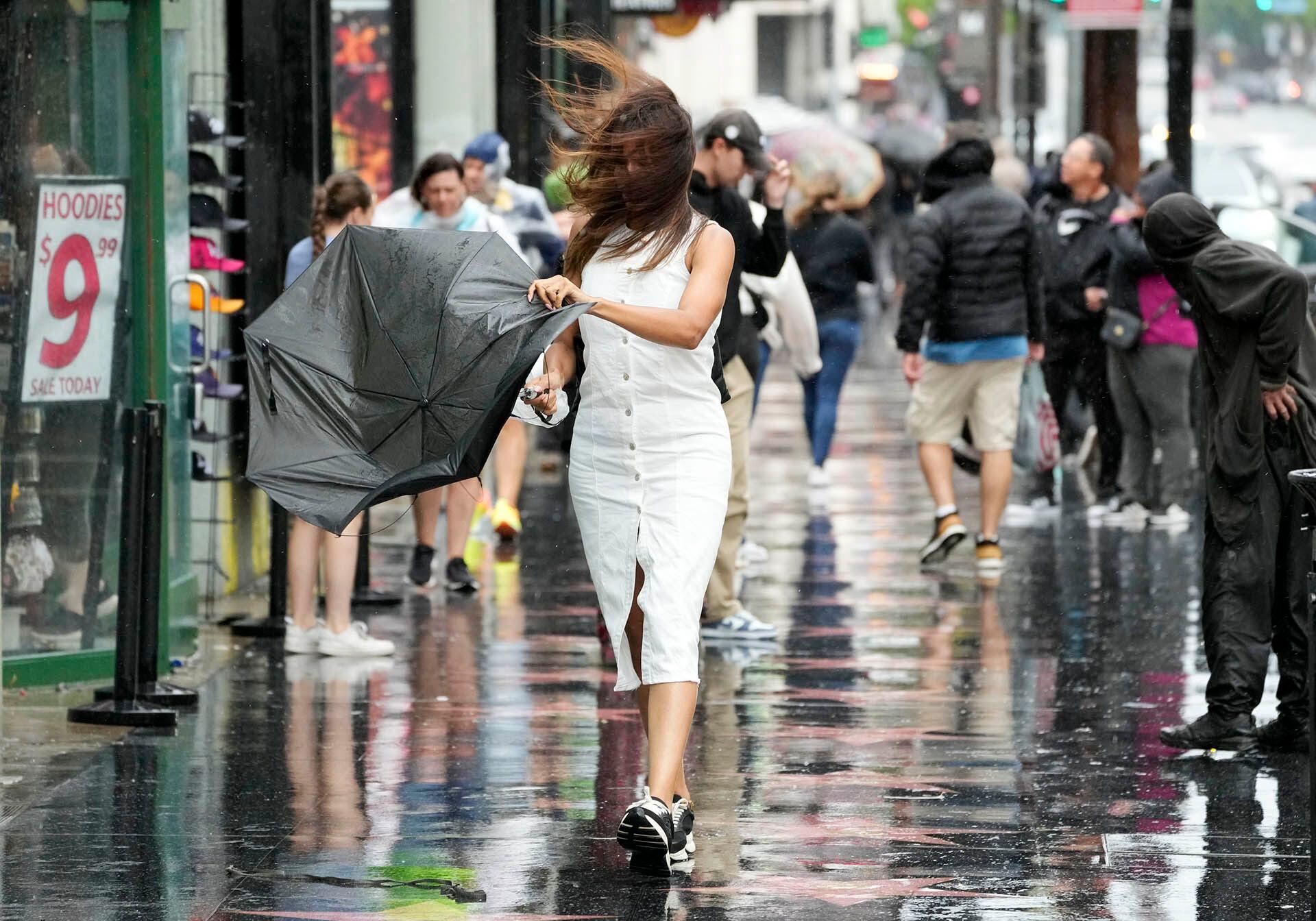 Una peatona atiende un paraguas roto mientras camina a través del viento y la lluvia en Hollywood Boulevard durante la tormenta tropical Hilary.