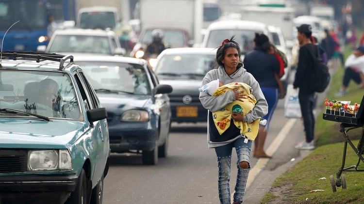 Una migrante venezolana, acunando a un bebé, camina por una avenida donde pide a los conductores su cambio de repuesto, en Bogotá, Colombia (Foto AP/Fernando Vergara)