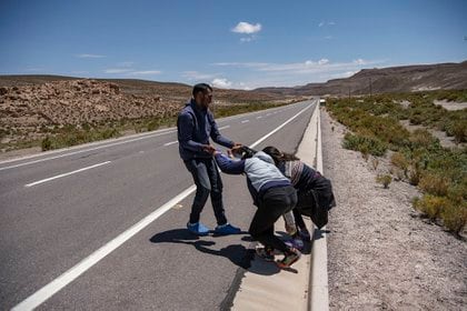 Un migrante ayuda a otras dos personas a levantarse luego de un descanso en medio de la caminata interminable (MARTIN BERNETTI / AFP)