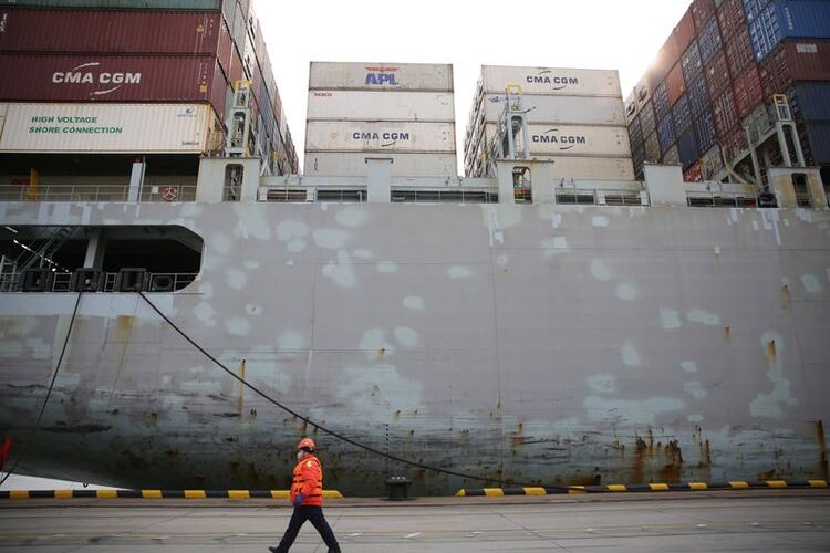 Un trabajador con una máscara facial pasa por delante de un buque de carga en una terminal de contenedores del puerto de Qingdao en la provincia de Shandong, China (Reuters)