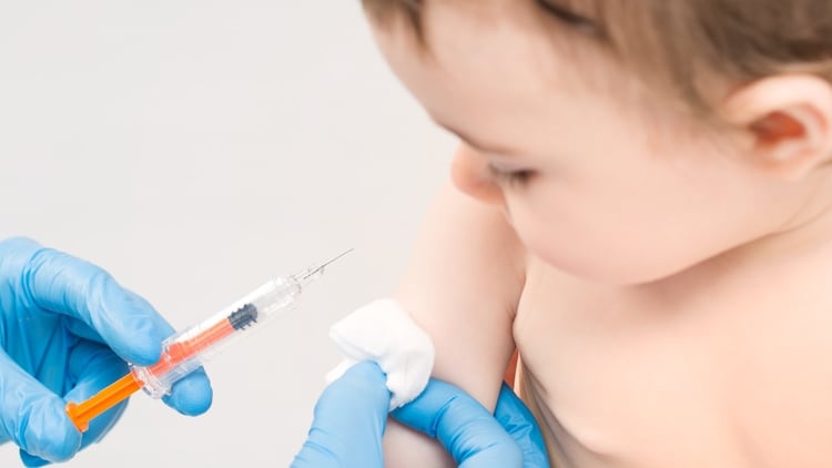Detalle de unas manos con guantes tocando el brazo de un bebé para aplicar vacuna