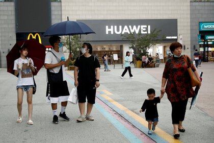 Paseantes chinos en tiempos de coronavirus, con fondo de MacDonalds y Huawei. Según Boldizzoni, lo de China no es capitalismo; el PC usa el mercado como mecanismo, dice, pero bajo estricto control político, que no deja espacio al "individualismo burgués" (Reuters) 