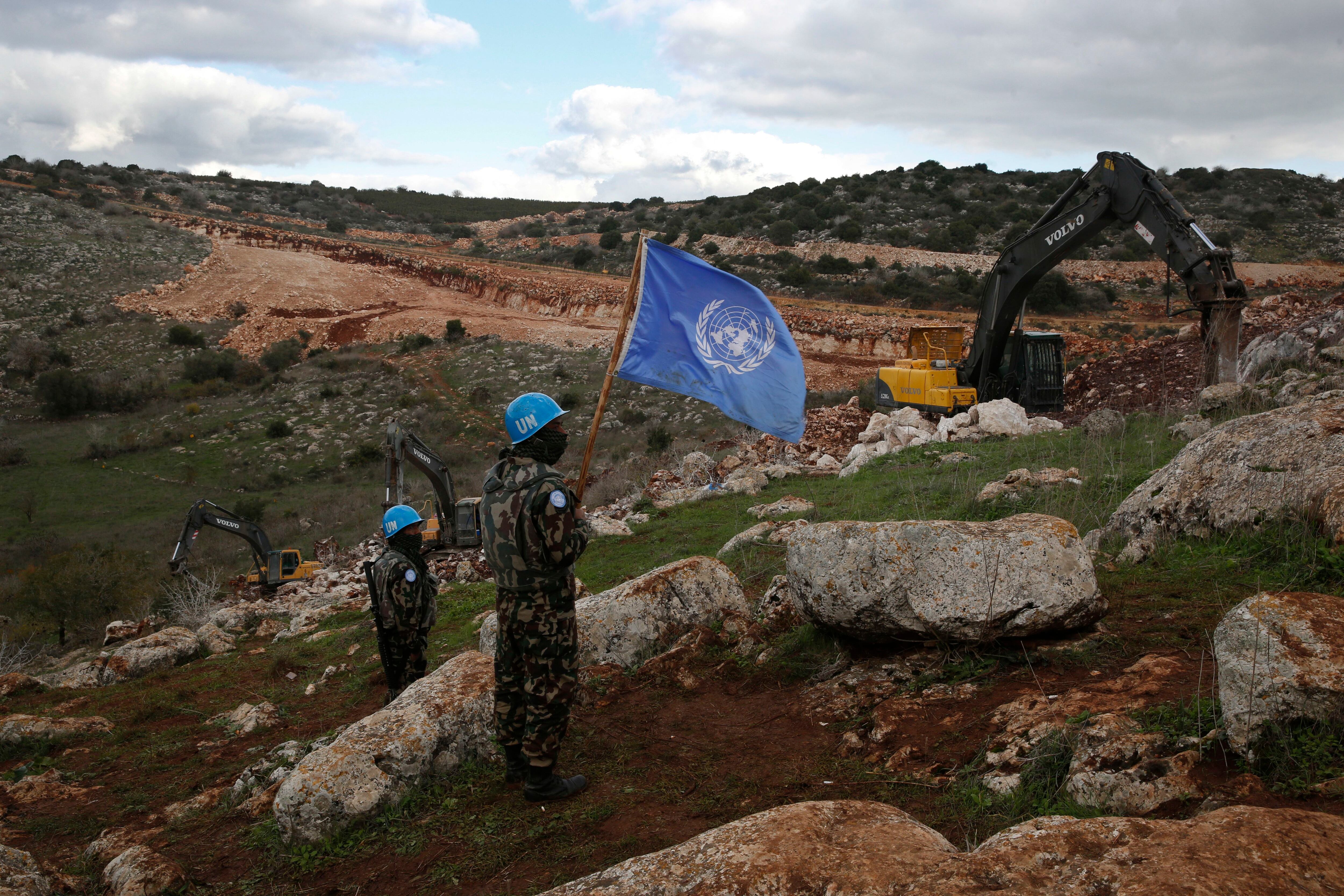 Efectivos de la misión de paz de Naciones Unidas sostienen su bandera mientras observan cómo las excavadoras israelíes tratan de destruir túneles construidos por Hezbollah, cerca de la localidad fronteriza de Mays al-Jabal, en Líbano (AP Foto/Hussein Malla, archivo)