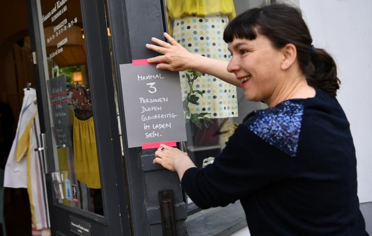 Babette Schumacher, vendedora de la tienda de ropa 'Frauen und Kinder zuerst', cuelga un letrero que indica el distanciamiento social en Berlín, Alemania, el 25 de abril de 2020. (REUTERS/Annegret Hilse)
