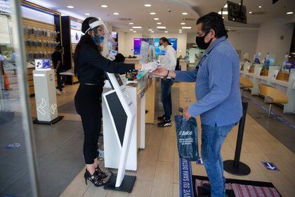 A mobile phone store employee wearing a mask and face shield to curb the spread of the new coronavirus tends to a client at a shop in the Polanco neighborhood of Mexico City, Thursday, July 30, 2020. Mexico's economic activity plummeted 18.9% in the second quarter compared to the same period last year as the economic shutdown caused by the COVID-19 pandemic drove the country deeper into a recession. (AP Photo/Marco Ugarte)