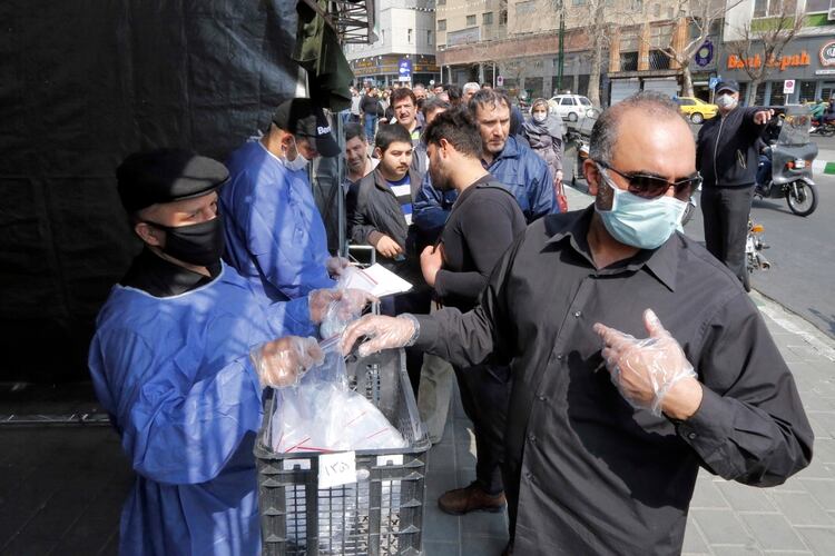 Milicianos Basiji entregan paquetes con elementos de protección contra el coronavirus a la salida de la estación del subte Meydane Valiasr de Teherán. (AFP)