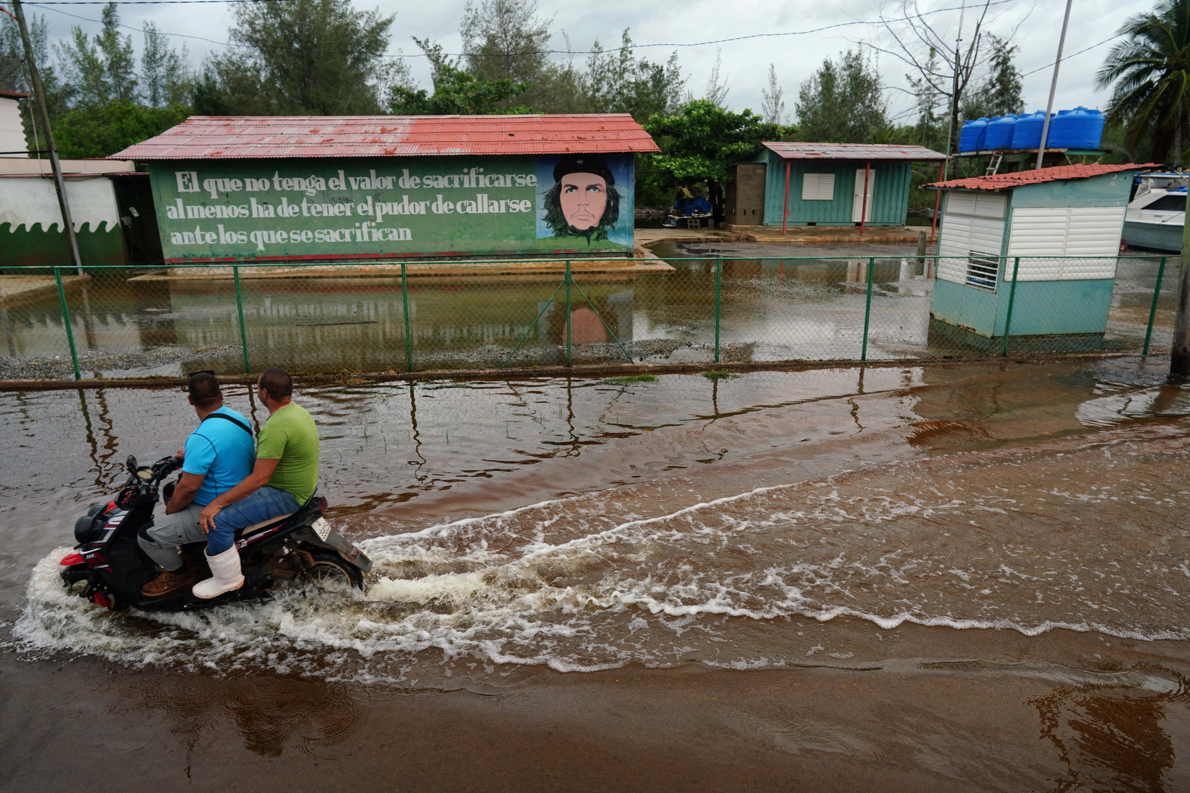 La gente en una calle inundada pasa junto a una imagen del difunto héroe revolucionario Ernesto 'Che' Guevara mientras la tormenta Idalia toca tierra en Cuba, en Guanimar, Cuba, el 28 de agosto de 2023. REUTERS/Alexandre Meneghini