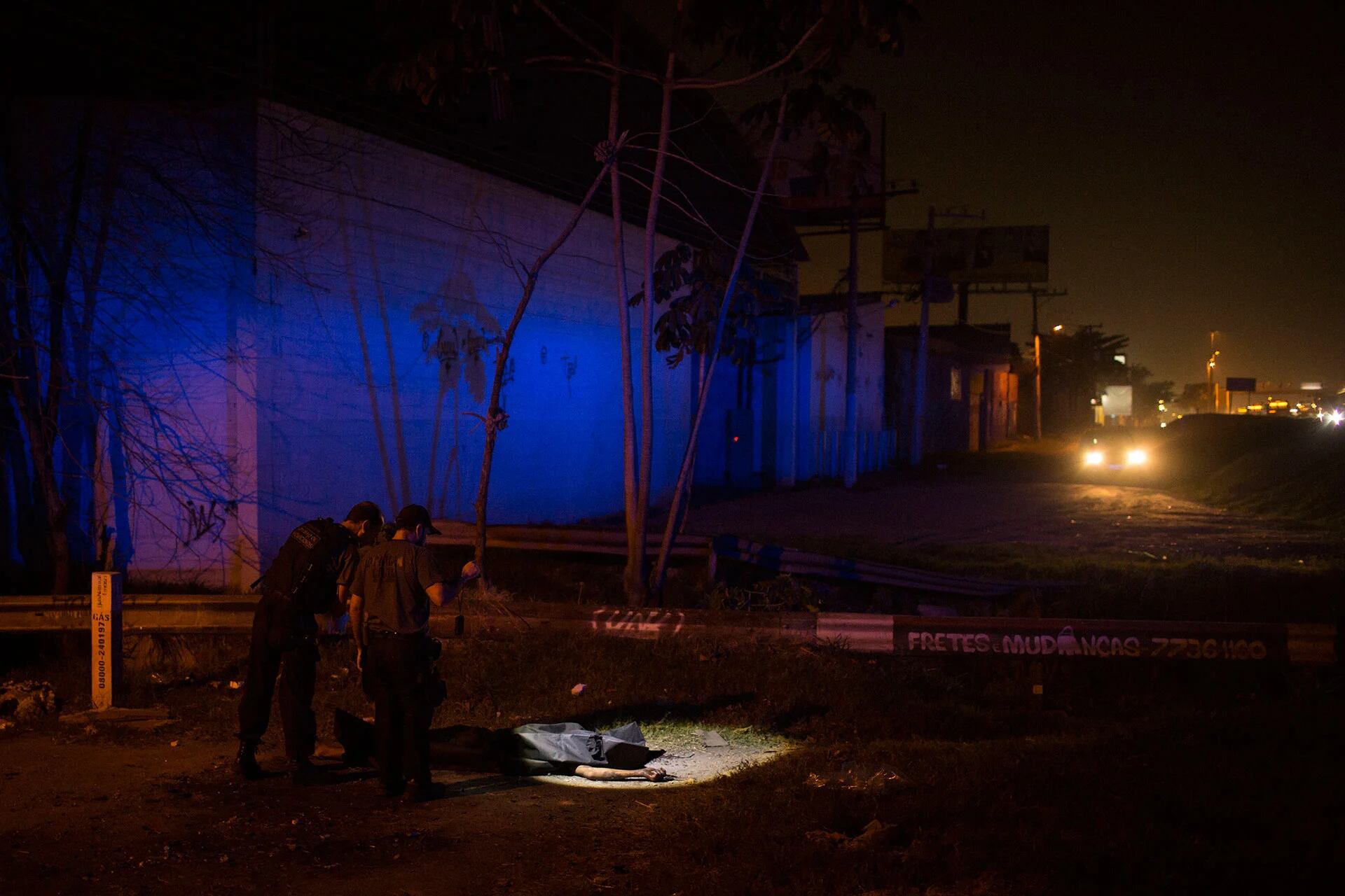 Dos oficiales de la policía observan el cuerpo de un joven asesinado en una guerra de pandillas (AP)