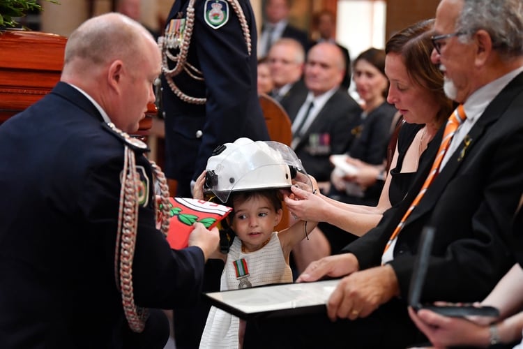 Charlotte O'Dwyer, la hija del voluntario del Servicio Rural de Bomberos Andrew O'Dwyer, con la esposa de Andrew Melissa, recibe el casco de su padre después de que el comisionado de RFS Shane Fitzsimmons le entregara la medalla de servicio de su padre durante su funeral en Our Lady of Victories Catholic Church en Horsley Park, Sydney, este martes 7 de enero de 2020. Andrew fue uno de los tantos héroes que intentan frenar el fuego en Australia (Reuters)