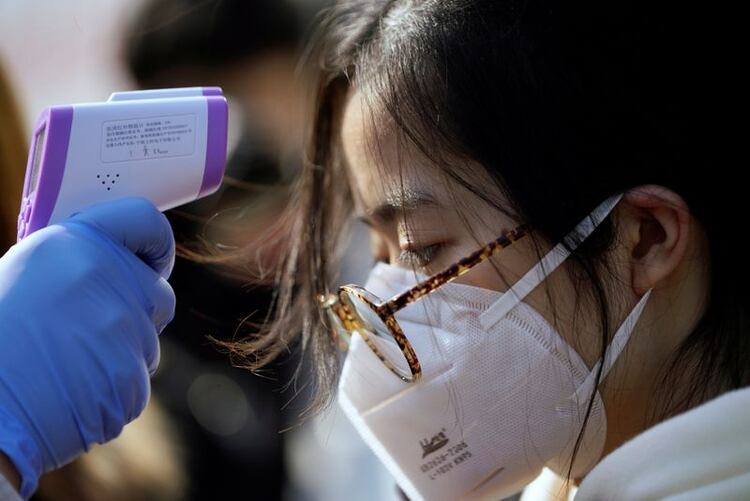Un trabajador le toma la temperatura a una mujer en una fábrica de Shanghai