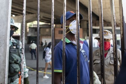 Una persona espera tras una valla de seguridad fuera de un hospital en Caracas (Bloomberg)