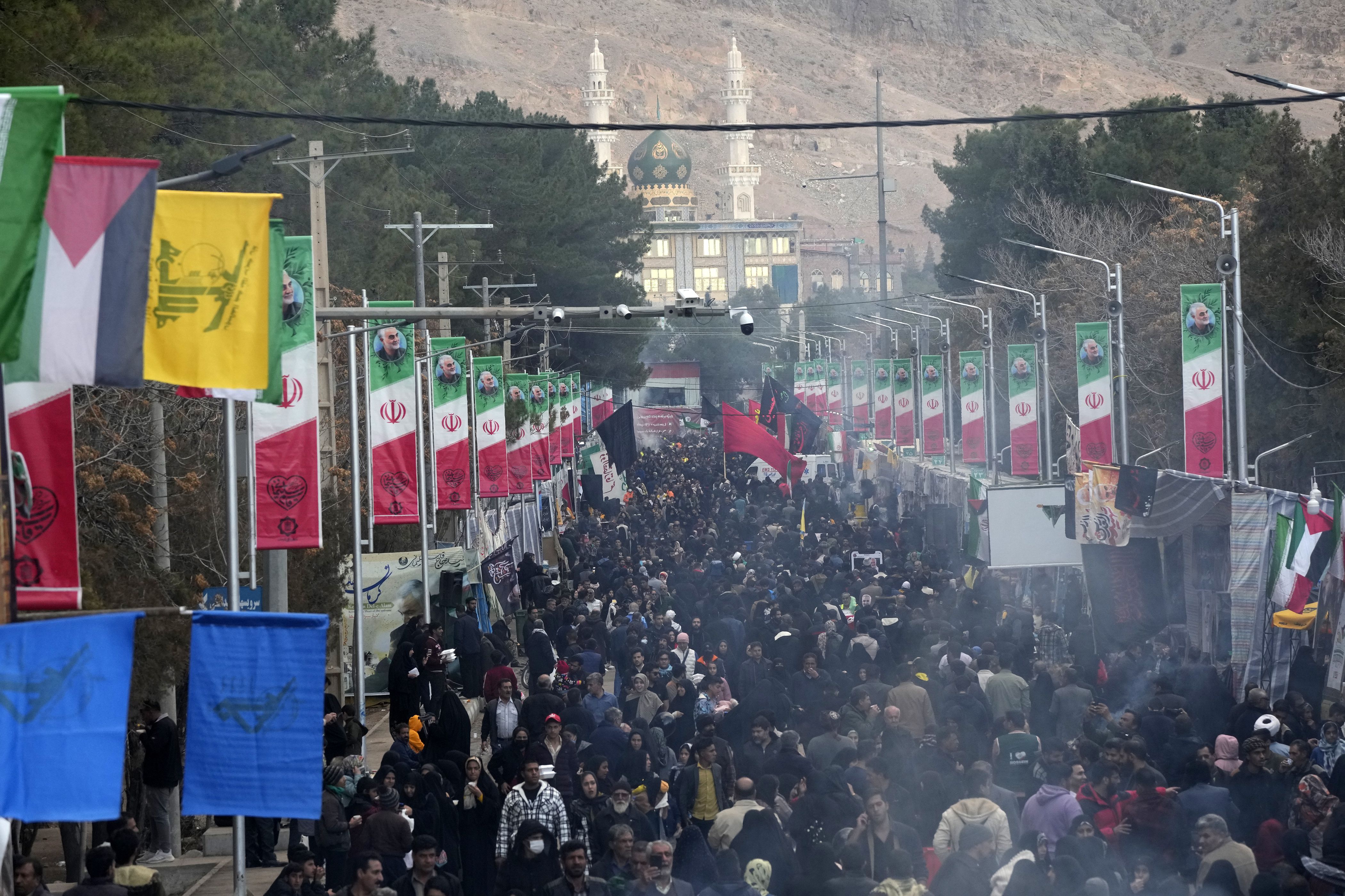 Una multitud de gente camina por una calle en dirección a la tumba del general Qassem Soleimani, general de la Guardia Revolucionaria de Irán, con una mezquita de fondo, en la ciudad de Kermán, a unos 820 kms (510 millas) al sureste de la capital, Teherán, el 4 de enero de 2024. (AP Foto/Vahid Salemi)