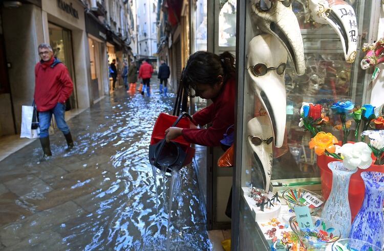 Una mujer vierte el agua de una tienda en un pasillo inundado en Venecia, Italia, el 14 de noviembre de 2019. (Reuters)