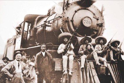 Soldados revolucionarios frente a un tren de vapor.